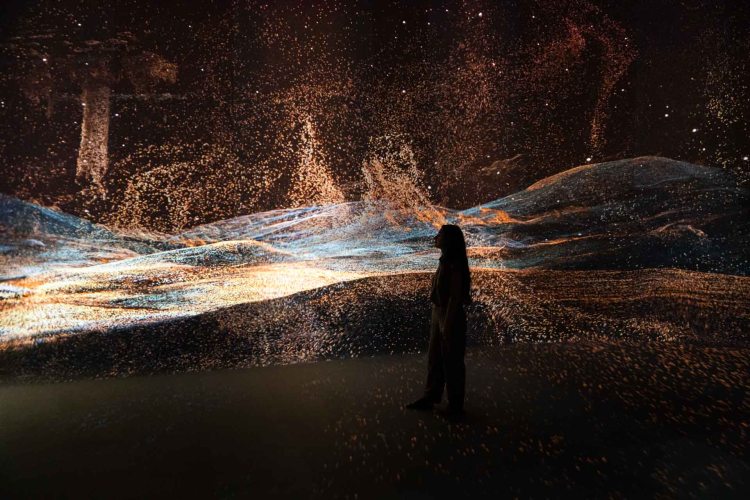 A woman walks in silhouette in front of projected colourful swirling particles.